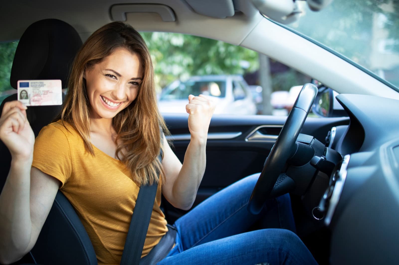 Lachende leerling in de auto met haar pas behaalde rijbewijs in de hand